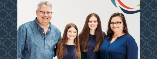a mother, father, and two daughters smile and pose for a photo