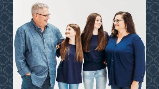 A family of four turn to each other while posing for a photo.