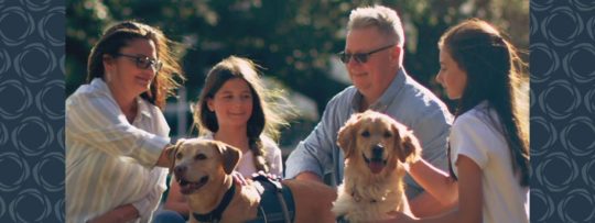 A family of four pets two dogs while sitting outdoors