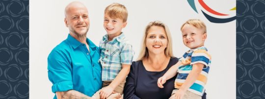 Two parents holding their two young boys while posing for a photo. 