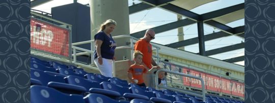 A family of four walk through bleachers at a baseball game.