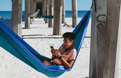 Young man in hammock under Pensacola Beach pier on smart phone.