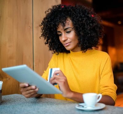 Person at a coffee shop with a credit car and reading a tablet