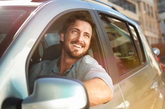 Man staring out car window with smile.