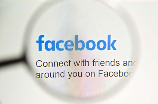 Facebook webpage with a magnifying glass focused on the Facebook logo.