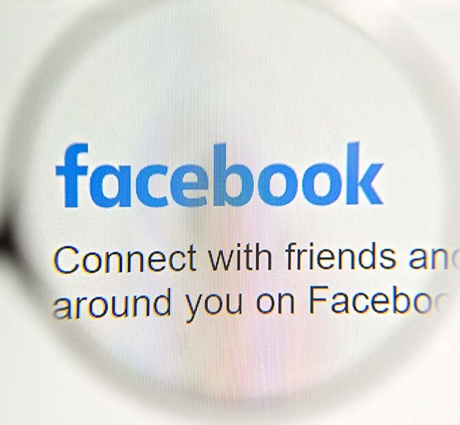 Facebook webpage with a magnifying glass focused on the Facebook logo.