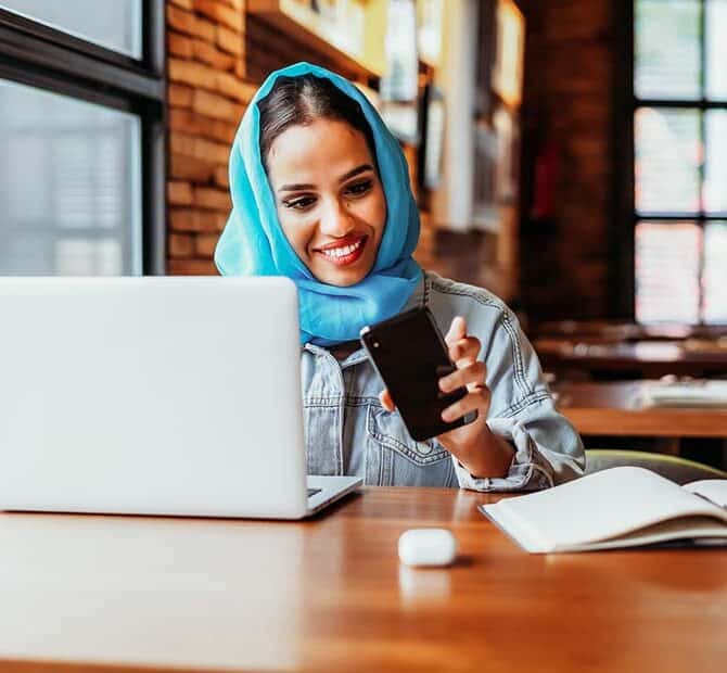woman at laptop looking at phone.