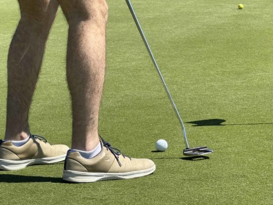 24th Annual Charity Golf Tournament - Golfer putts ball to hole on green.