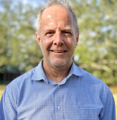 man in blue shirt standing in front of trees