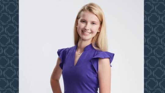 A young woman wearing a purple dress poses for a photo.