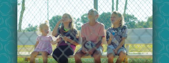 four children sit on a bench behind a fence 