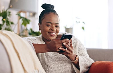 Woman smiles while checking her phone on a couch