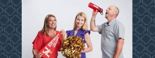 A family of three pose for a picture with college merchandise. 