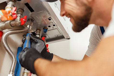 Closeup of plumber using screwdriver while installing new steel hot water central heating system in apartment