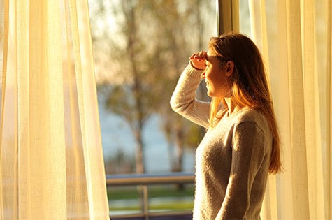 Happy teen scouting through a window at home